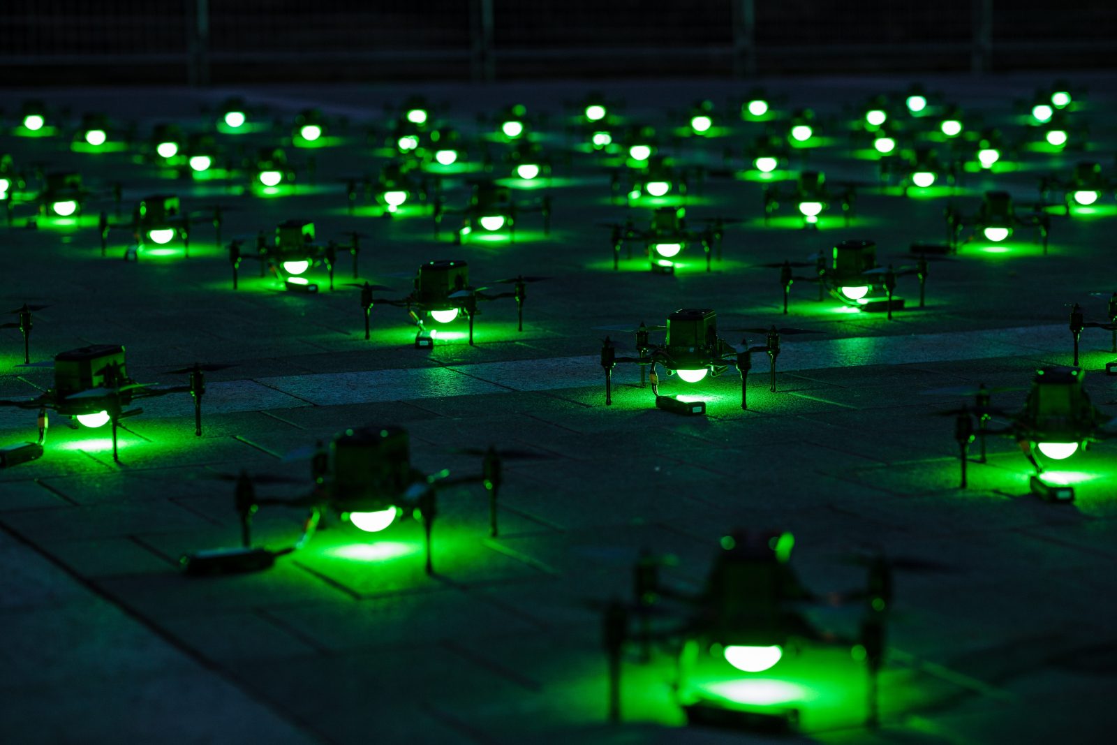Lighted drone swarm for light show sits on the ground, poised for takeoff and lit